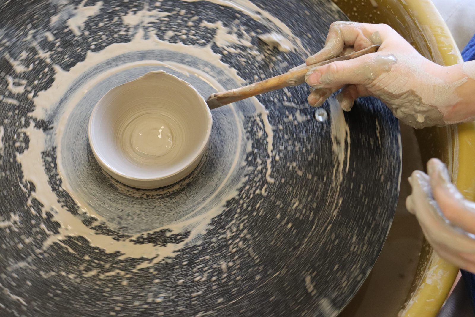 Small hands trimming a bowl on the pottery wheel