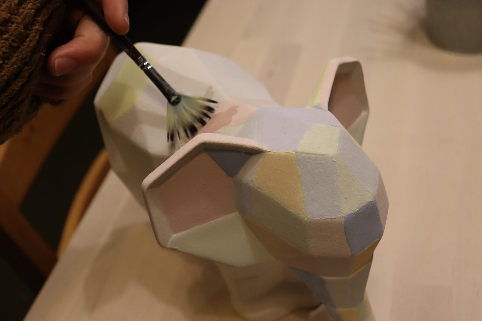 A hand painting a pastel geometric elephant pottery piece