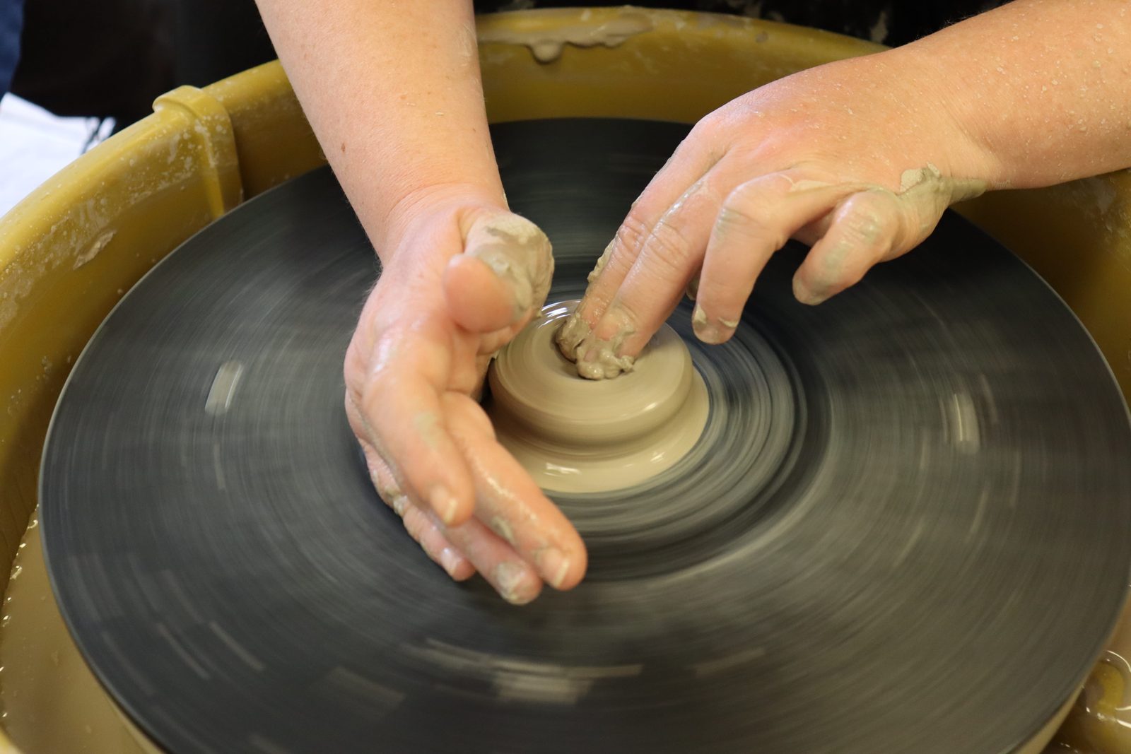 Hands centering a ball of clay on a spinning pottery wheel